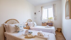 Ein Schlafzimmer mit zwei Betten, einem Fenster mit Vorhängen, einem Nachttisch mit Lampe und einem Spiegel an der Wand.