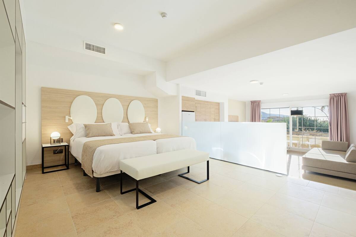 A modern bedroom with a large bed, bedside tables, a bench, and a balcony with a view.
