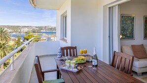 Un balcon avec une table en bois mise pour le petit-déjeuner, comprenant des fruits, des boissons et une bouteille de champagne.
