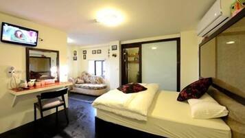 Habitación de hotel con cama, escritorio, silla, televisor y aire acondicionado.