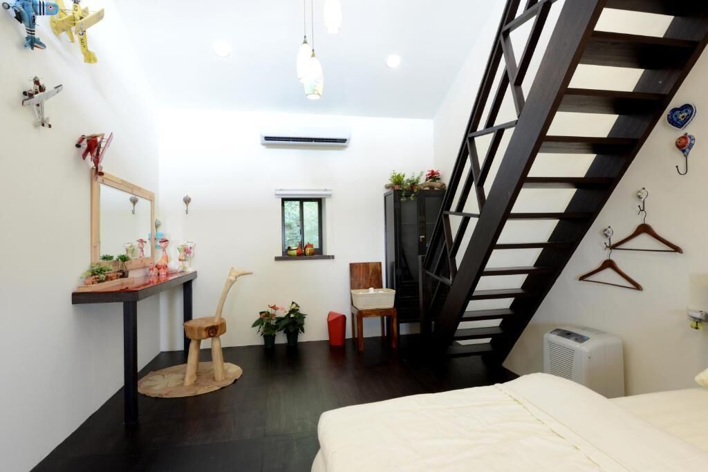 Quarto com cama, escrivaninha com espelho, cadeira, janela pequena e escada.