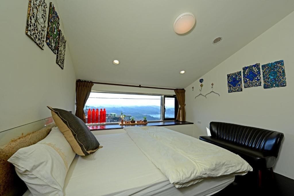 Een hotelkamer met een bed, een zwarte leren bank, een groot raam met uitzicht en kunstwerken aan de wanden.