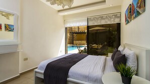 Un dormitorio moderno con una cama, una mesita con una planta, vista a una piscina y obras de arte en la pared.