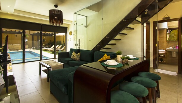 Una sala de estar moderna con un sofá verde, una mesa de centro de vidrio y una escalera que lleva a un baño.