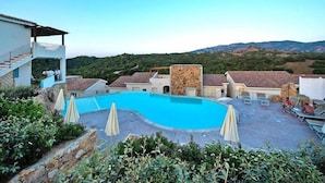 A swimming pool surrounded by buildings with a view of hills. - Apartment in Golfo Aranci with elevator (Baja Sardinia (SS))