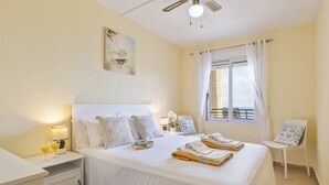 Habitación de hotel con una cama grande, una mesita de noche con lámpara, una silla y una ventana con cortinas.