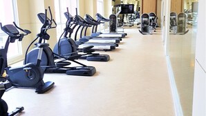 A gym with multiple treadmills lined up along a corridor, large windows, and exercise equipment in the background. - Grande Caribbean Resort - Sleeps 2 (Pattaya)
