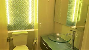 A bathroom with a toilet, a glass sink, and a mirror.