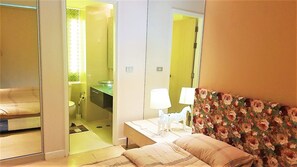A hotel room with a bed, a nightstand, a mirror, and a bathroom visible through an open door.