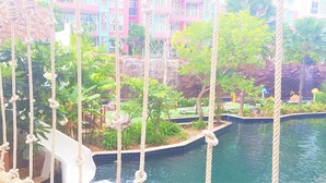 A pool area with ropes, greenery, and a building in the background. - Grande Caribbean Resort - Sleeps 2 (Pattaya)