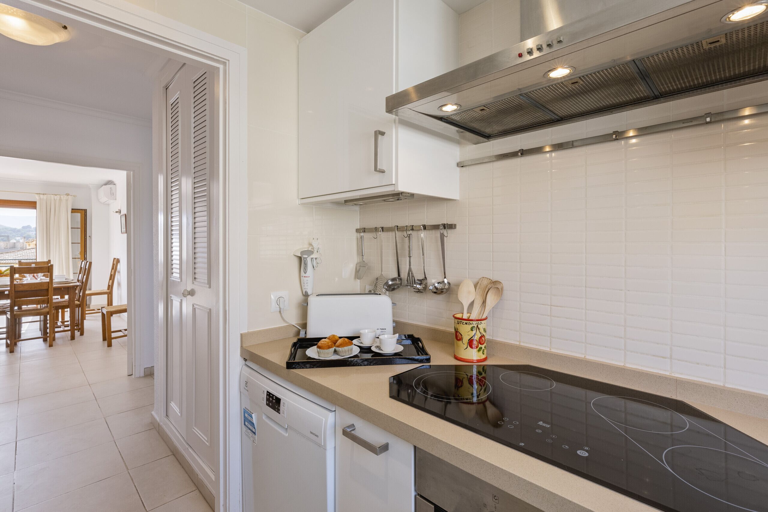 A modern kitchen with white cabinets, a built-in oven, and a dining area with wooden furniture.