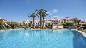 Una grande piscina con palme e un edificio sullo sfondo con diversi balconi.