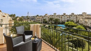 Un balcone con mobili in vimini, una piscina e vista su una zona residenziale con palme e edifici.