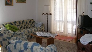 A living room with a sofa, two armchairs, a coffee table, a television, and a lace-curtained window. - Apartments Violeta (Liznjan)