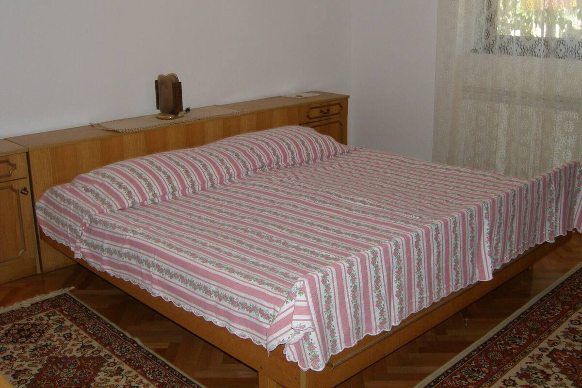 A single-bed room with a wooden headboard, a bedside table with a lamp, and a patterned rug on the floor.
