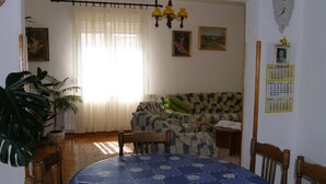 A living room with a sofa, a dining table with a blue floral tablecloth, a chandelier, and a wall calendar. - Apartments Violeta (Liznjan)