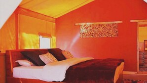 A bedroom with a wooden bed, a window with curtains, and a patterned wall hanging. - Nubra Organic Retreat - Hunder - Campsite (Leh)