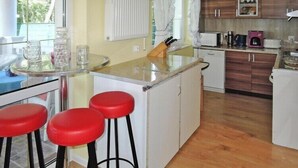 A compact kitchen with a wooden floor, a small island with stools, a white refrigerator, and a microwave. - New holiday home in Nowe Warpno for 6 persons (Nowe Warpno)