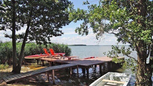 A dock with a small boat, a red surfboard, and a lounge chair by the water. - New holiday home in Nowe Warpno for 6 persons (Nowe Warpno)