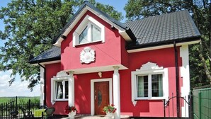 A red house with a white door, two windows, and a small porch with chairs. - New holiday home in Nowe Warpno for 6 persons (Nowe Warpno)