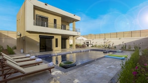 A modern two-story house with a swimming pool, lounge chairs, and a patio area.