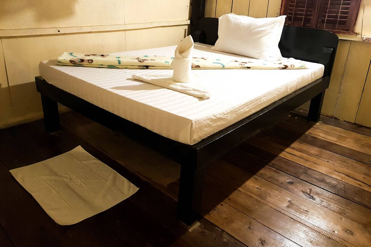 A single bed with a white mattress, a black headboard, and a wooden floor.