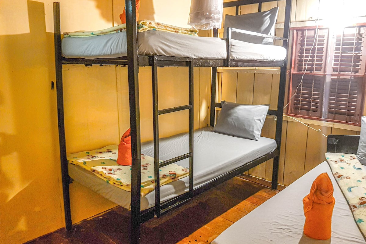 A bunk bed with a mattress and pillows, a wooden floor, and a window with blinds.