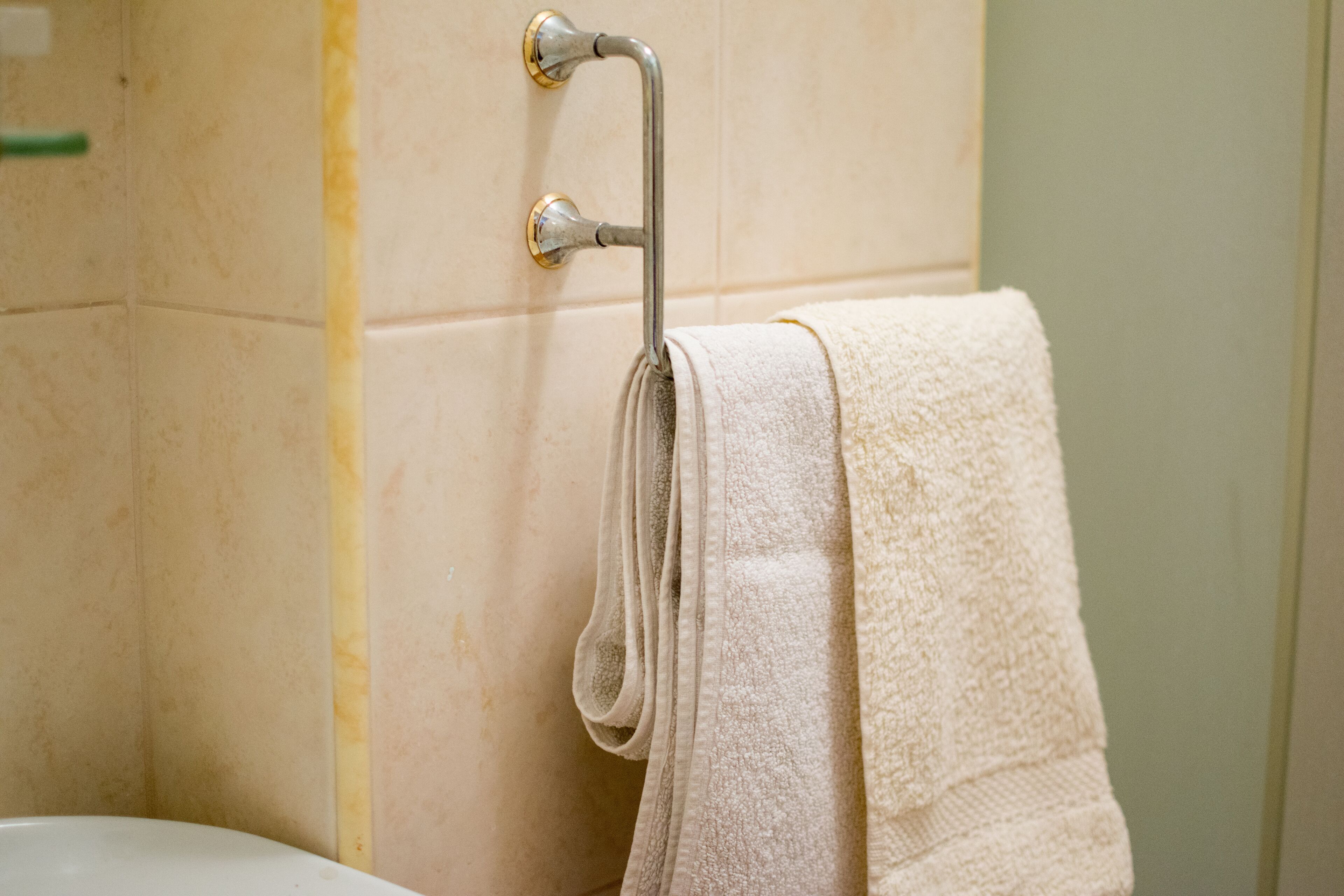 Un baño con una bañera blanca, un perchero con una toalla doblada y paredes de baldosas color beige.