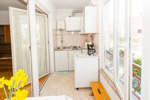 Uma cozinha compacta com pia, fogão e geladeira, um banco de madeira e uma janela com vista para o verde.