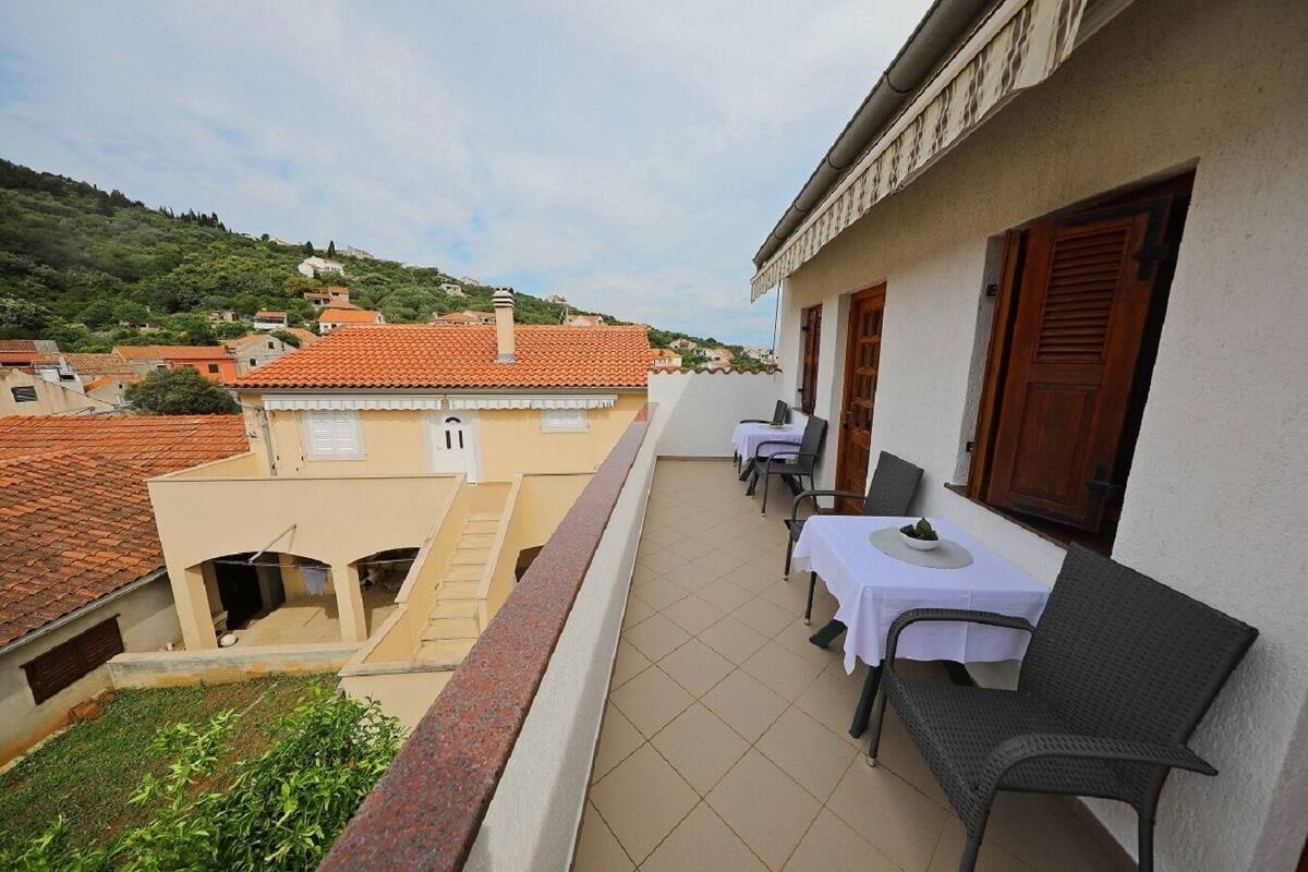 A balcony with a table and chairs, a view of the town, and a building with a red-tiled roof.
