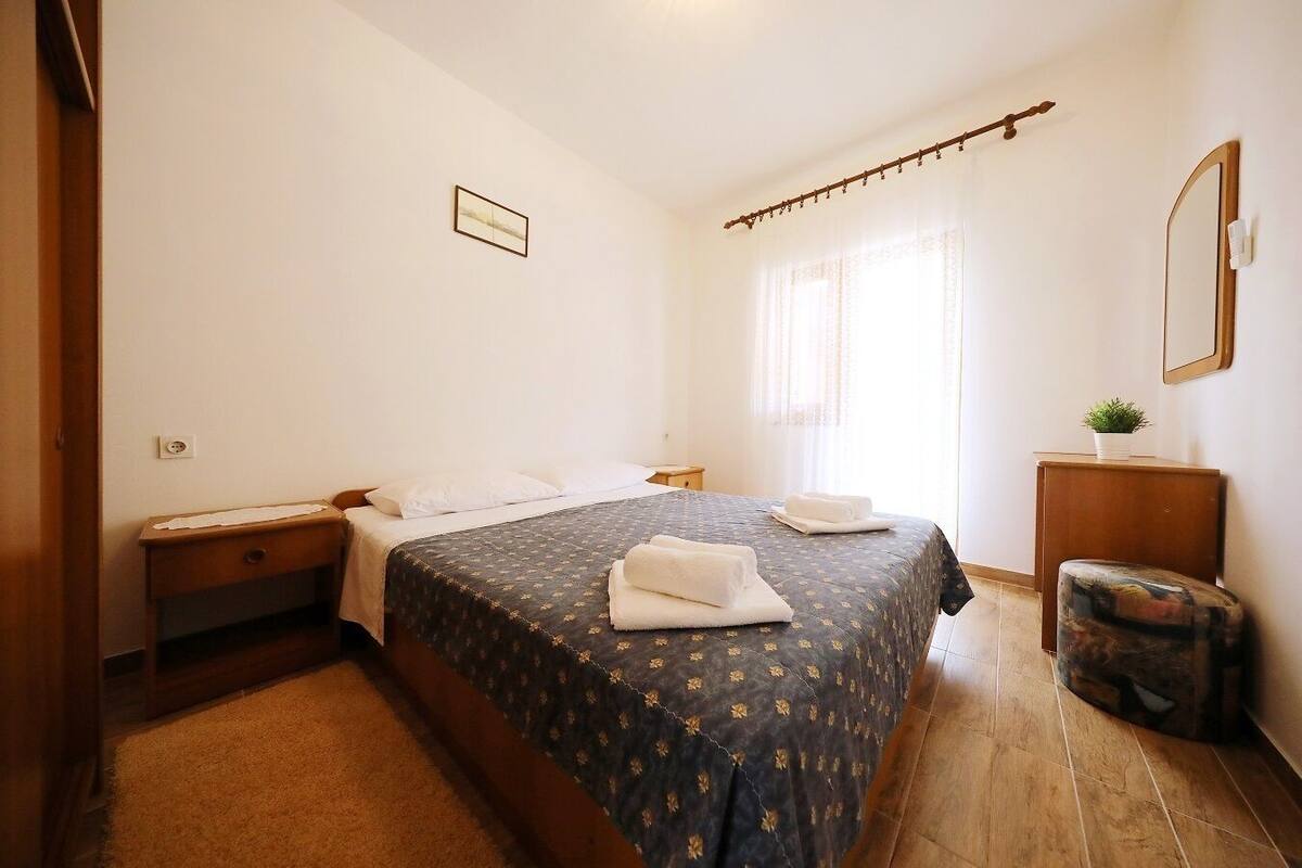 A bedroom with a bed, a nightstand, a small table, a mirror, and a potted plant.