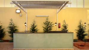 Ein überdachter Außenbereich mit Glastrennwand, Kübelpflanzen, Wandleuchten und einem Feuerlöscher.