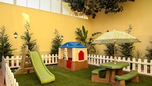 Ein Kinderspielbereich mit Rutsche, einem kleinen Haus und Picknicktischen.