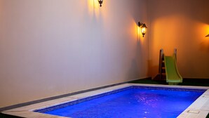 A small indoor pool with blue lighting, a slide, and a green chair. - Villa Naya Branch 5 Saray (Al Rama)