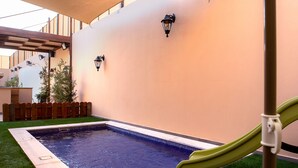 A poolside area with a green slide, a wooden fence, and a peach-colored wall. - Villa Naya Branch 5 Saray (Al Rama)