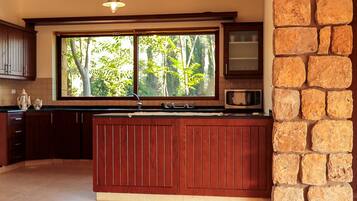 Cocina con armarios de madera, pared decorativa de piedra, ventana con vistas a árboles y un microondas.