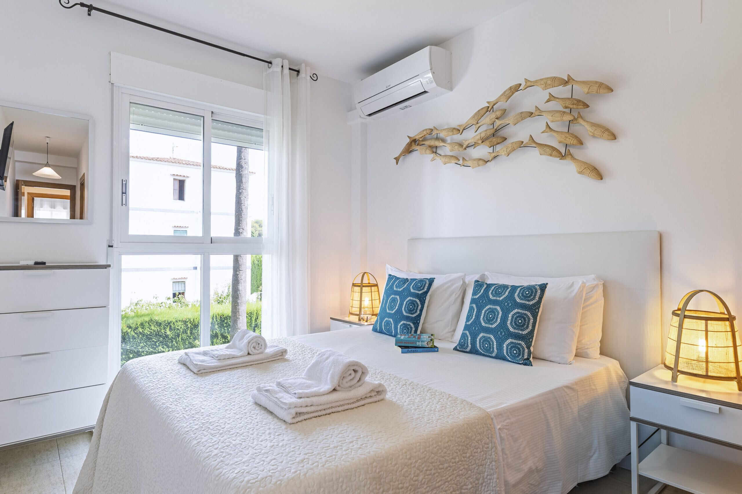 Quarto de hotel com uma cama grande, duas mesas de cabeceira, ar condicionado na parede e vista para o verde lá fora.