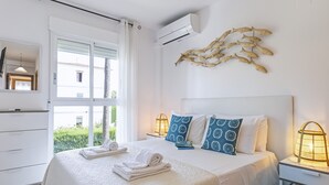 Quarto de hotel com uma cama grande, duas mesas de cabeceira, ar condicionado na parede e vista para o verde lá fora.