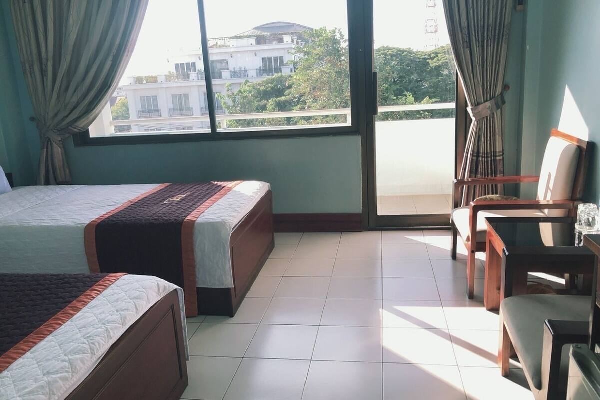 Habitación de hotel con dos camas, un balcón y una zona de estar con sillas y una mesa.