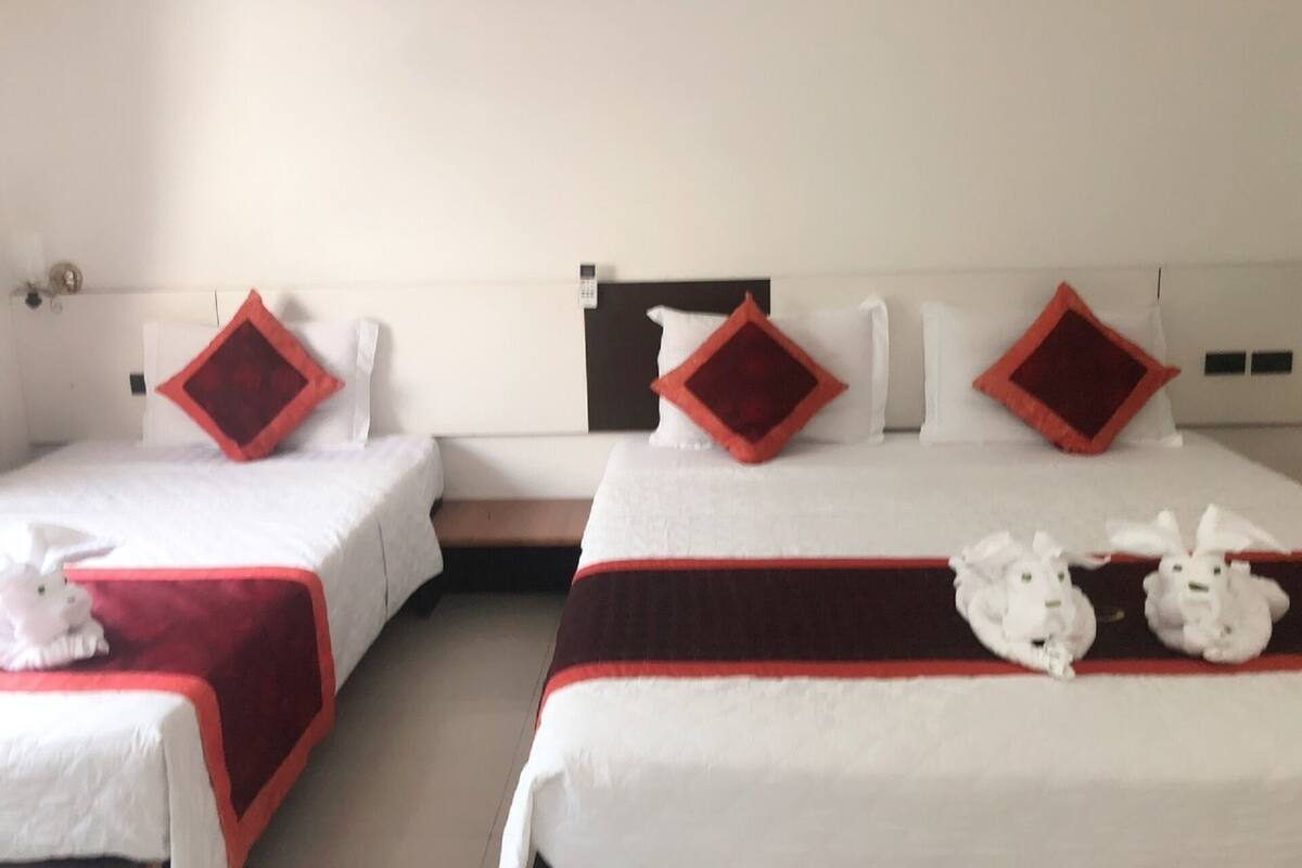 Habitación de hotel con dos camas individuales, cada una con almohada roja y blanca, y una cama grande con colcha roja y blanca.