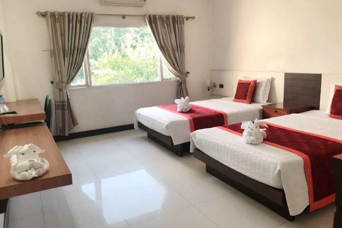 Habitación de hotel con dos camas, un escritorio de madera y un ventanal con cortinas.