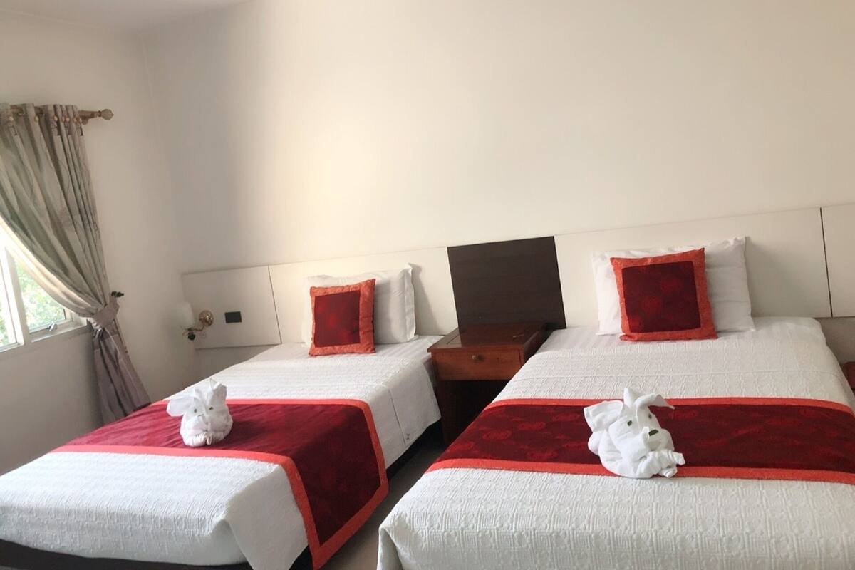 Una habitación de hotel con dos camas, cada una con una colcha roja y blanca, y una mesita de noche de madera entre ellas.