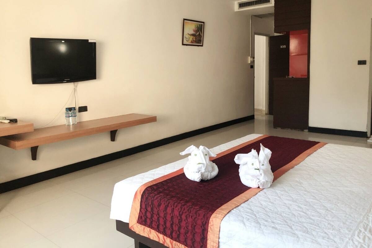 Habitación de hotel con una cama, un televisor montado en la pared, un banco de madera y una puerta que da a otra habitación.