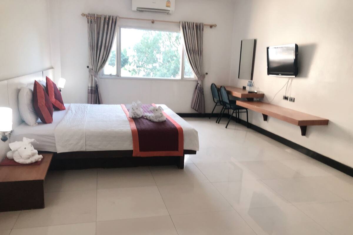 Una habitación de hotel con cama, escritorio, silla, televisión y ventana con cortinas.