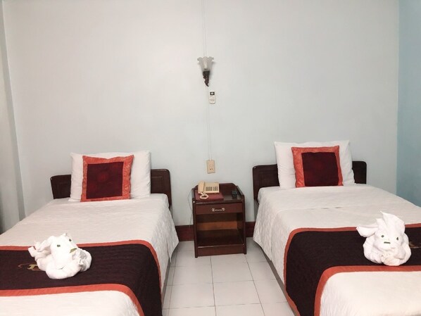 A hotel room with two beds, each with a red and white bedspread, a small bedside table with a telephone, and a wall-mounted light fixture.