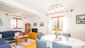 Un salon comprenant un canapé, une table basse et un coin repas avec des chaises et une table. On y trouve également un téléviseur, un meuble et des œuvres d’art accrochées aux murs.