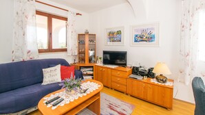 Un salon avec un canapé bleu, un meuble en bois, une télévision et une table sur laquelle sont posées des télécommandes.