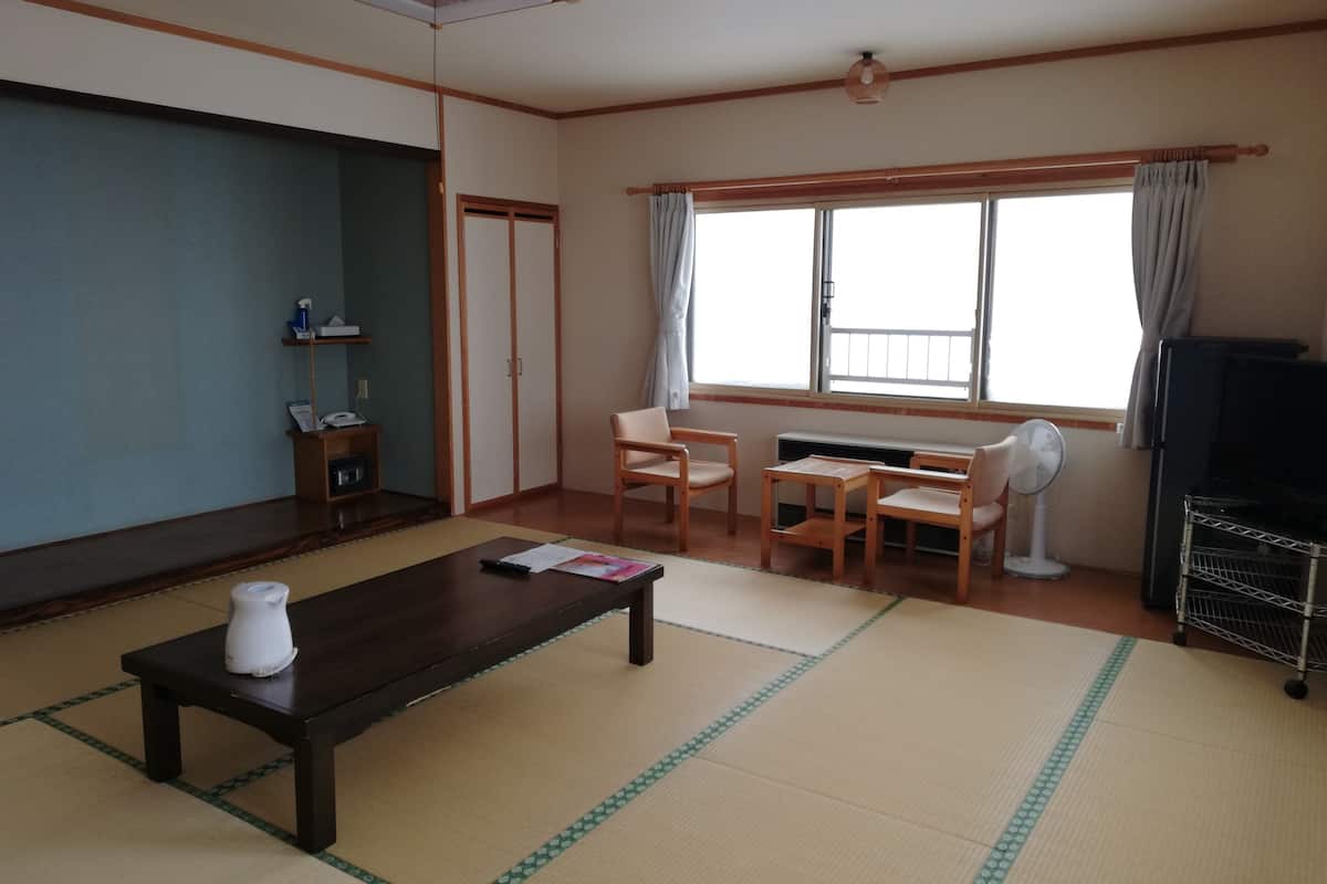 A living room with tatami mats, a dark wooden coffee table, a sofa, a TV, and a fan.
