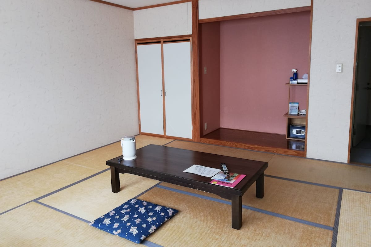 A traditional Japanese room with tatami flooring, a low wooden table, a blue cushion, and sliding doors.