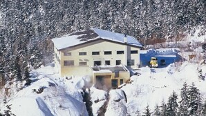 Un edificio con varias ventanas y un tejado cubierto de nieve, rodeado de árboles y nieve.